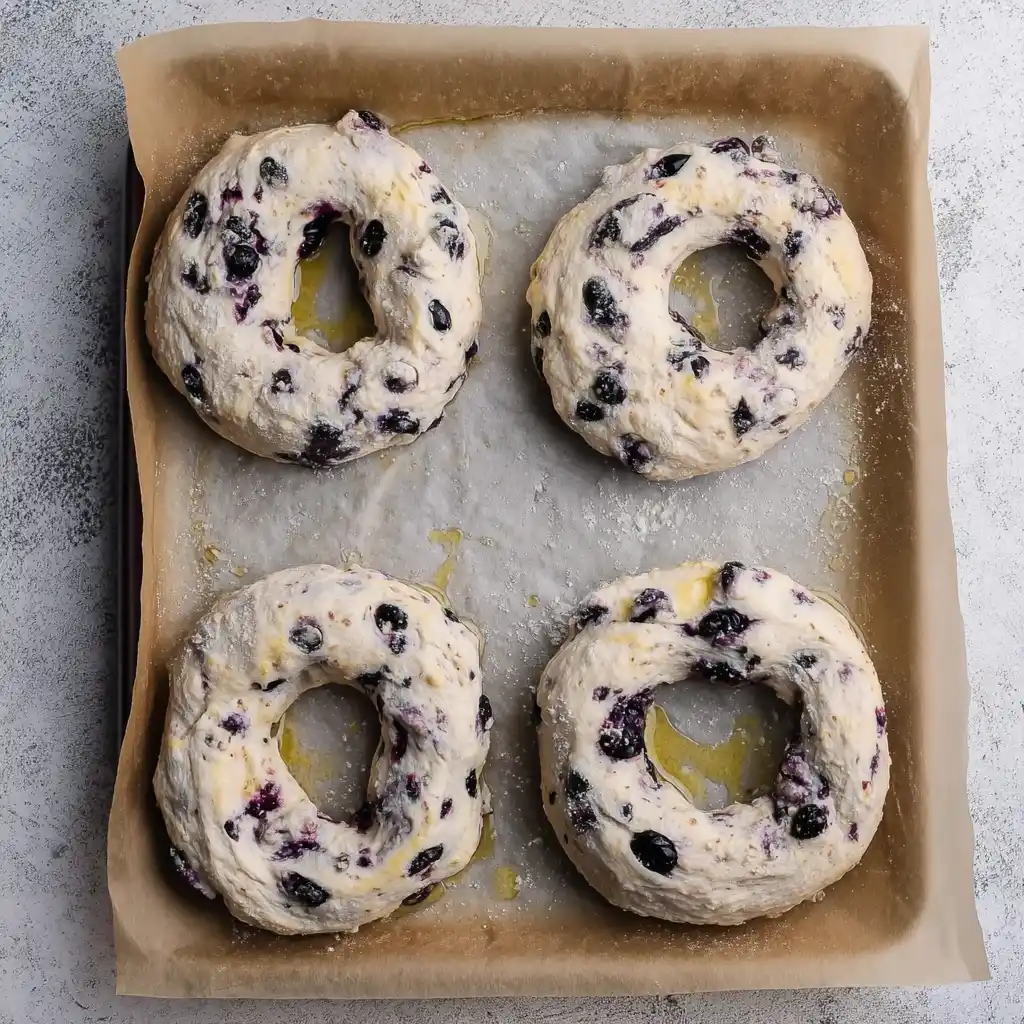 Unbaked blueberry bagels shaped and placed on parchment-lined baking tray