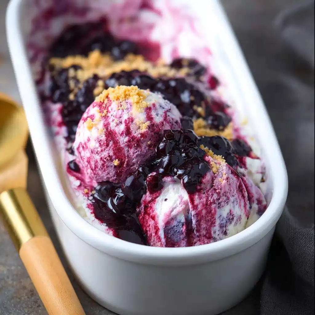 blueberry cheesecake ice cream in a container with blueberry swirl and graham cracker crumbs