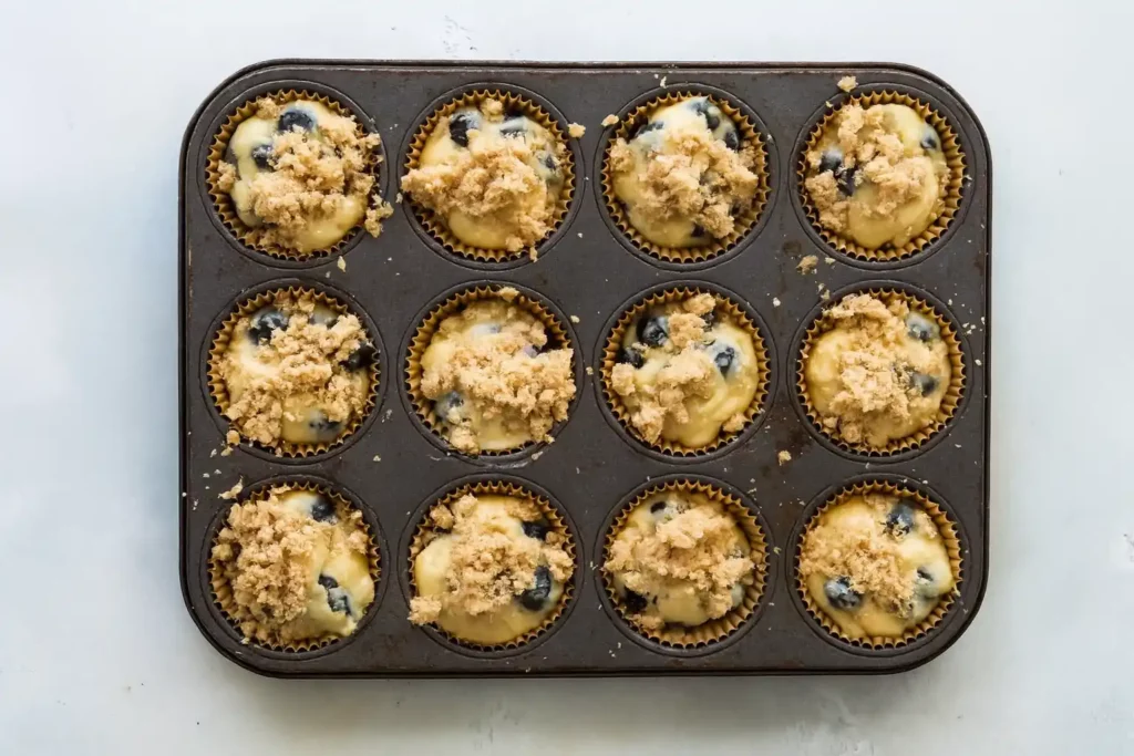 Blueberry muffin batter in paper-lined muffin tin, ready to bake