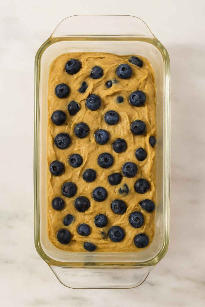 Banana bread batter topped with fresh blueberries in a glass loaf pan