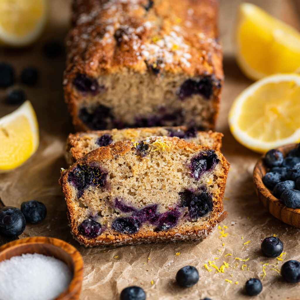 Lemon blueberry banana bread sliced on parchment with fresh lemons and blueberries